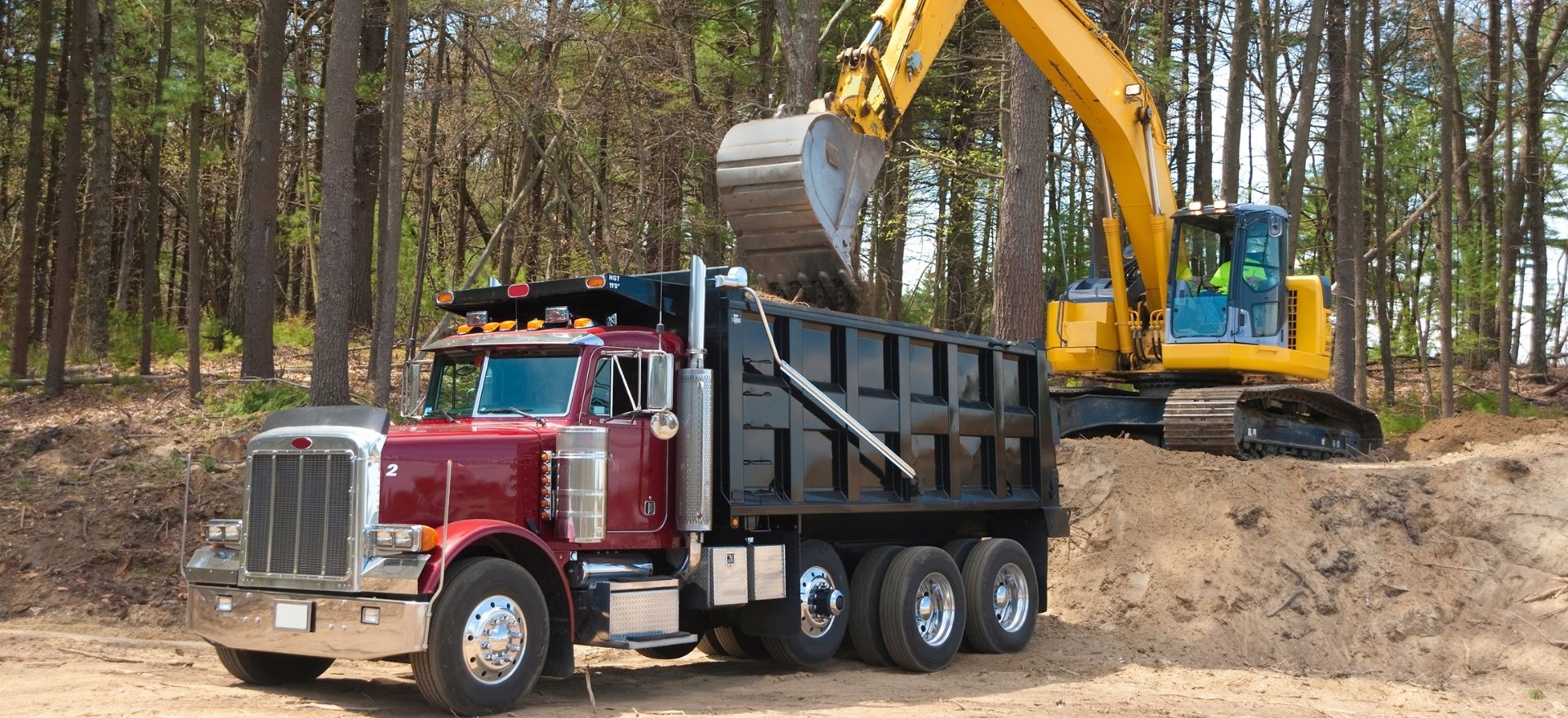 Dump truck being field with dirt by a backhoe